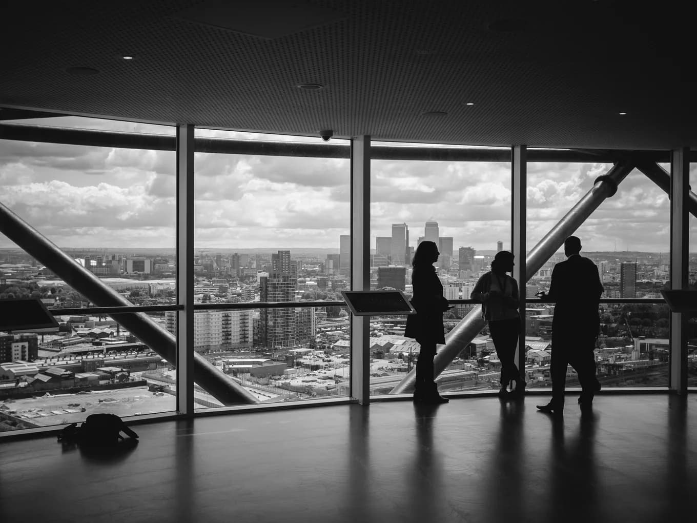 Three people talking at a window above a city, in silhouette.